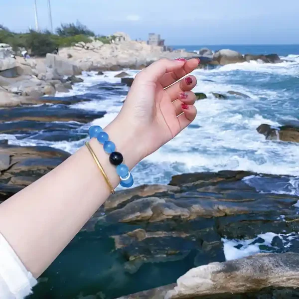 Wrist shot of aquamarine and blue tiger eye bracelet by the ocean