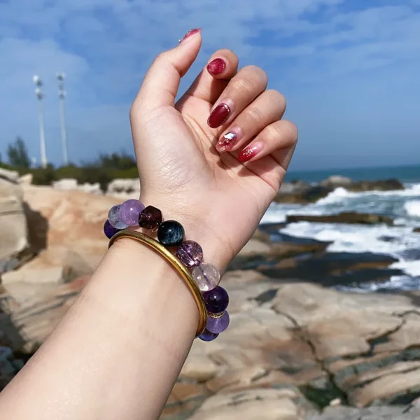 Woman’s hand raised against ocean background wearing amethyst smoky quartz bracelet