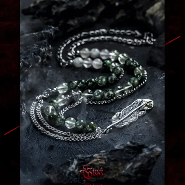 Green phantom crystal necklace with silver feather pendant laid on stone