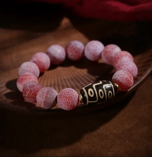 Pink agate bracelet with nine-eye Dzi bead on wooden tray
